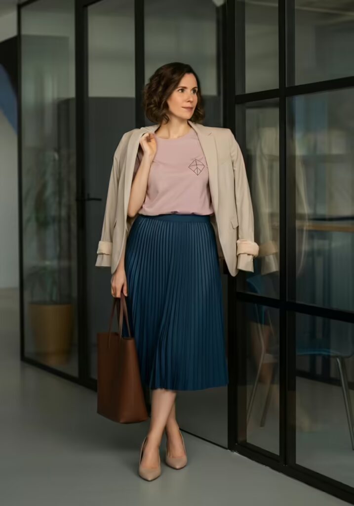 10 Minimalist T-Shirt Style Ideas for a Clean & Modern Look 14 A woman in a modern office wearing a minimalist tee tucked into a pleated skirt with a blazer.