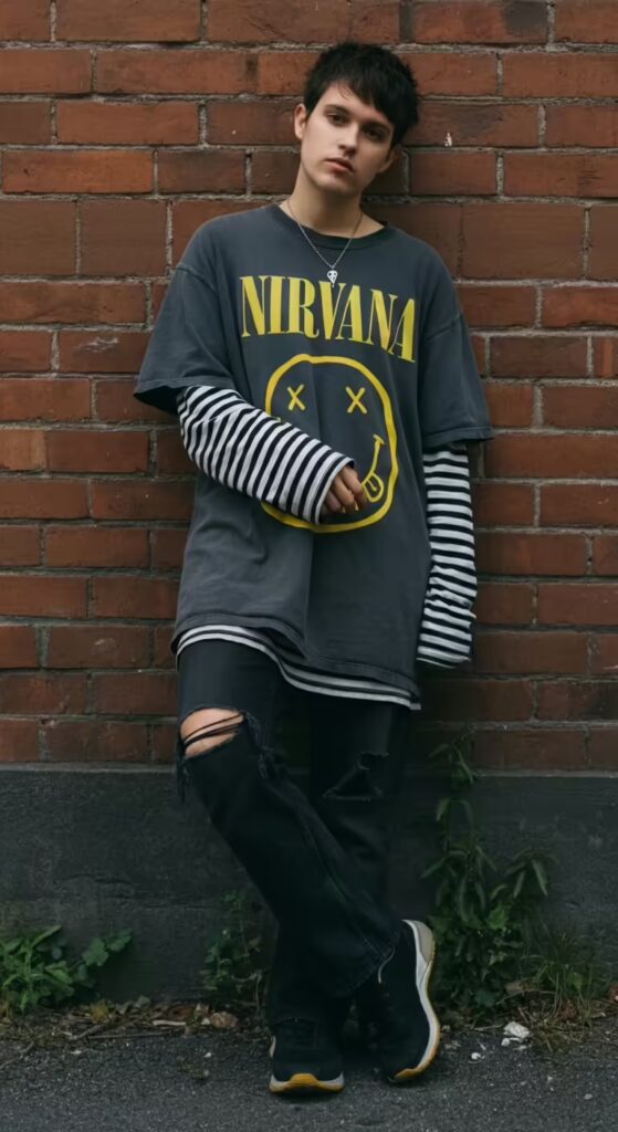 Oversized vs Regular Fit: 10 Style Ideas to Master Both T-Shirt Fits 8 A teenager with a 90s grunge style, wearing a short-sleeve oversized band tee over a striped long-sleeve shirt.