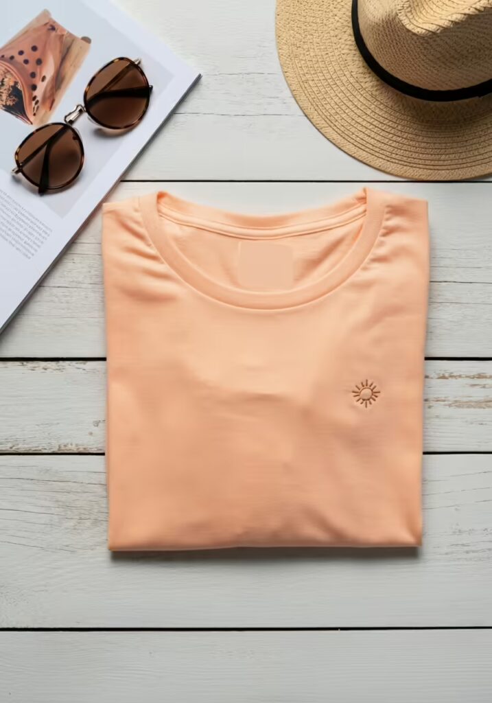 Summer T-Shirt Ideas to Refresh Your Warm-Weather Style 4 A flat lay of a peach-colored t-shirt with sunglasses and a straw hat